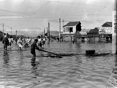 水没した大通りを膝まで水に浸かって行き交う人々の白黒写真