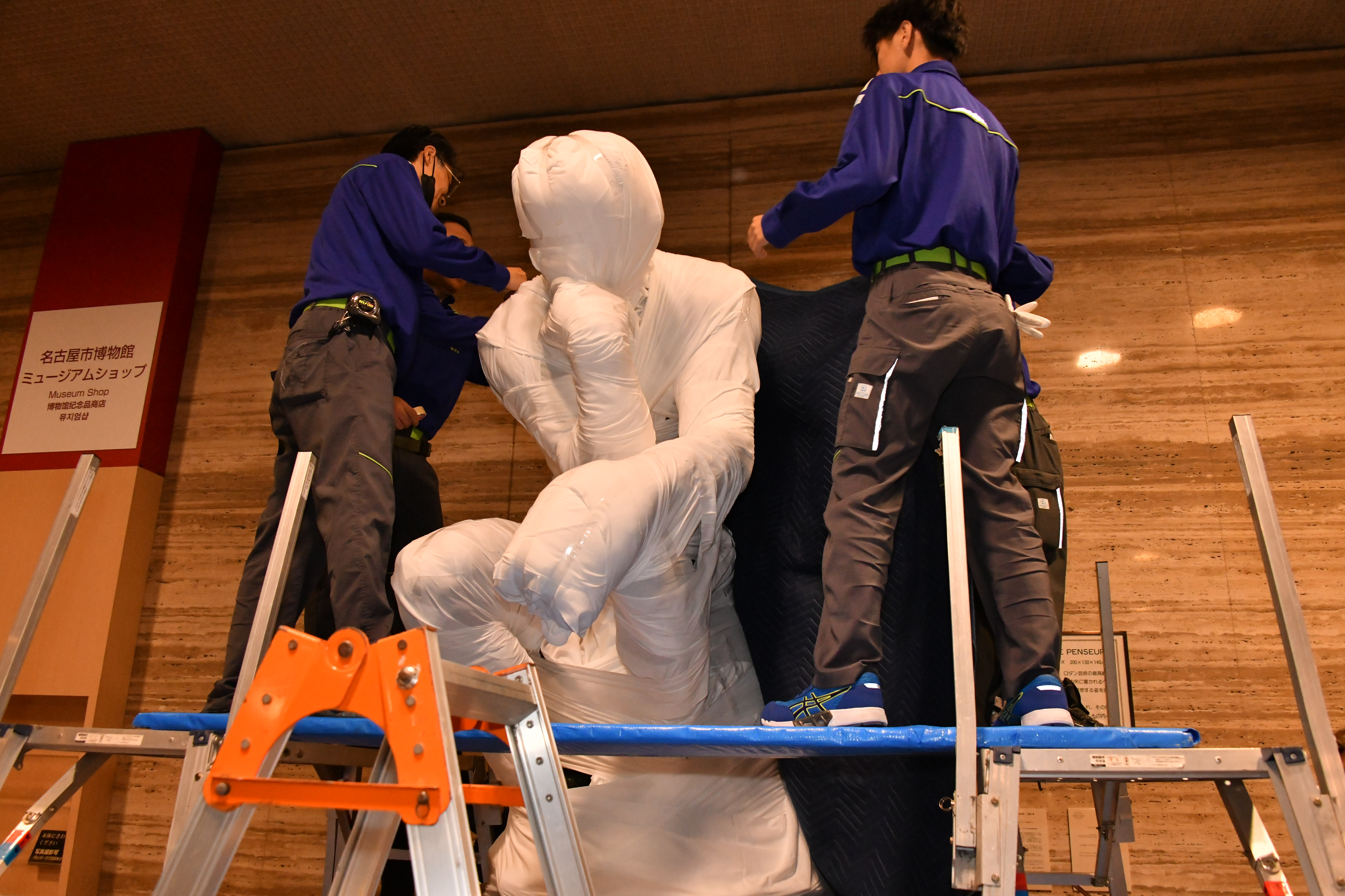 ｢考える人｣像を白い布で巻いていく2人の作業員