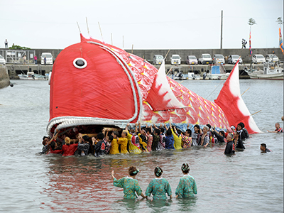海の中で若者たちが鯛の形をした神輿を担いでいる写真