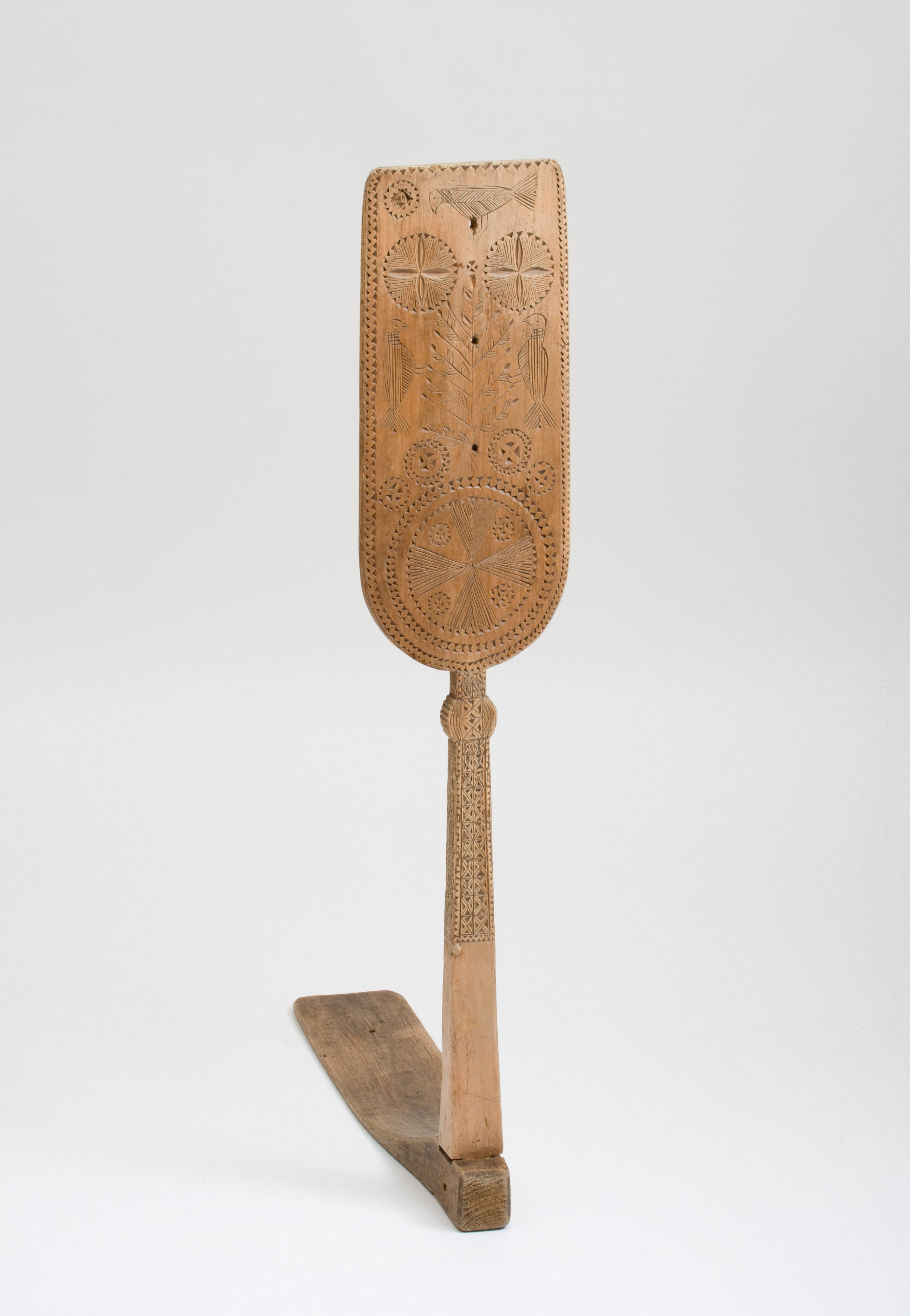 Patterns of birds and stars are carved onto a wooden rod with a flat, board-like top