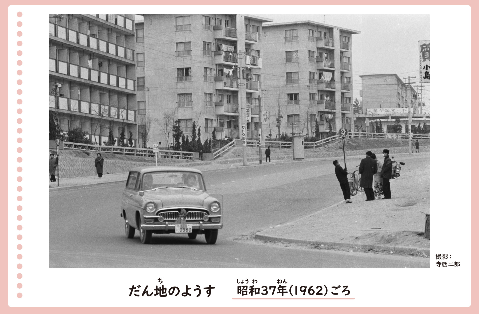 団地が立ち並ぶ風景。団地のそばの道路には車が走り、歩道では人々が歩いたり集まって話したりしている。