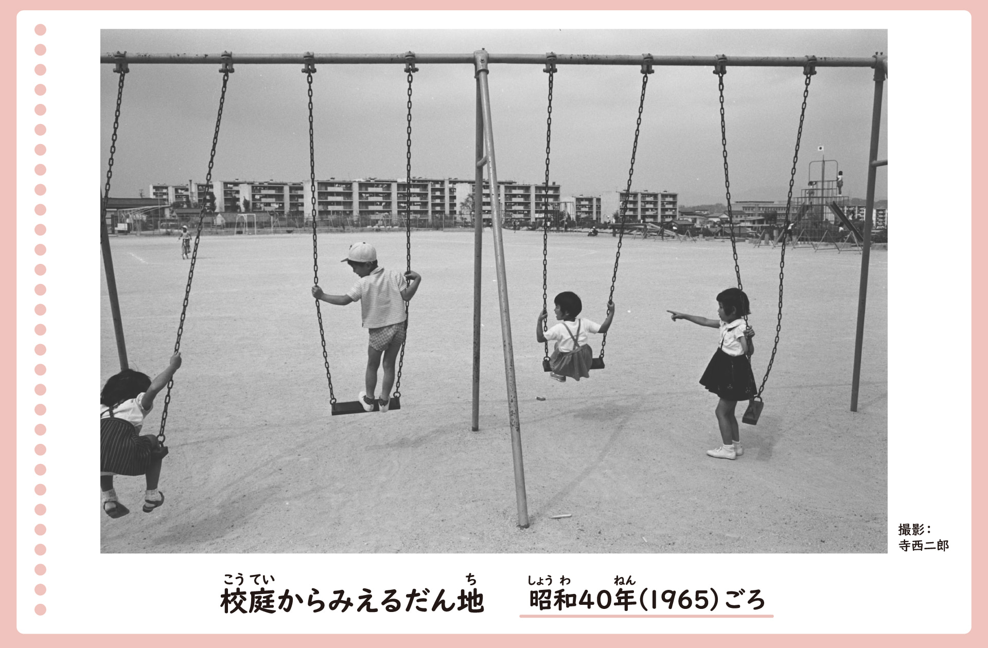 校庭のブランコからみえる団地の風景。学校の校庭にあるブランコで子どもたちが遊んでいる。その向こうには多くの団地が立ちならんでいるのがみえる。